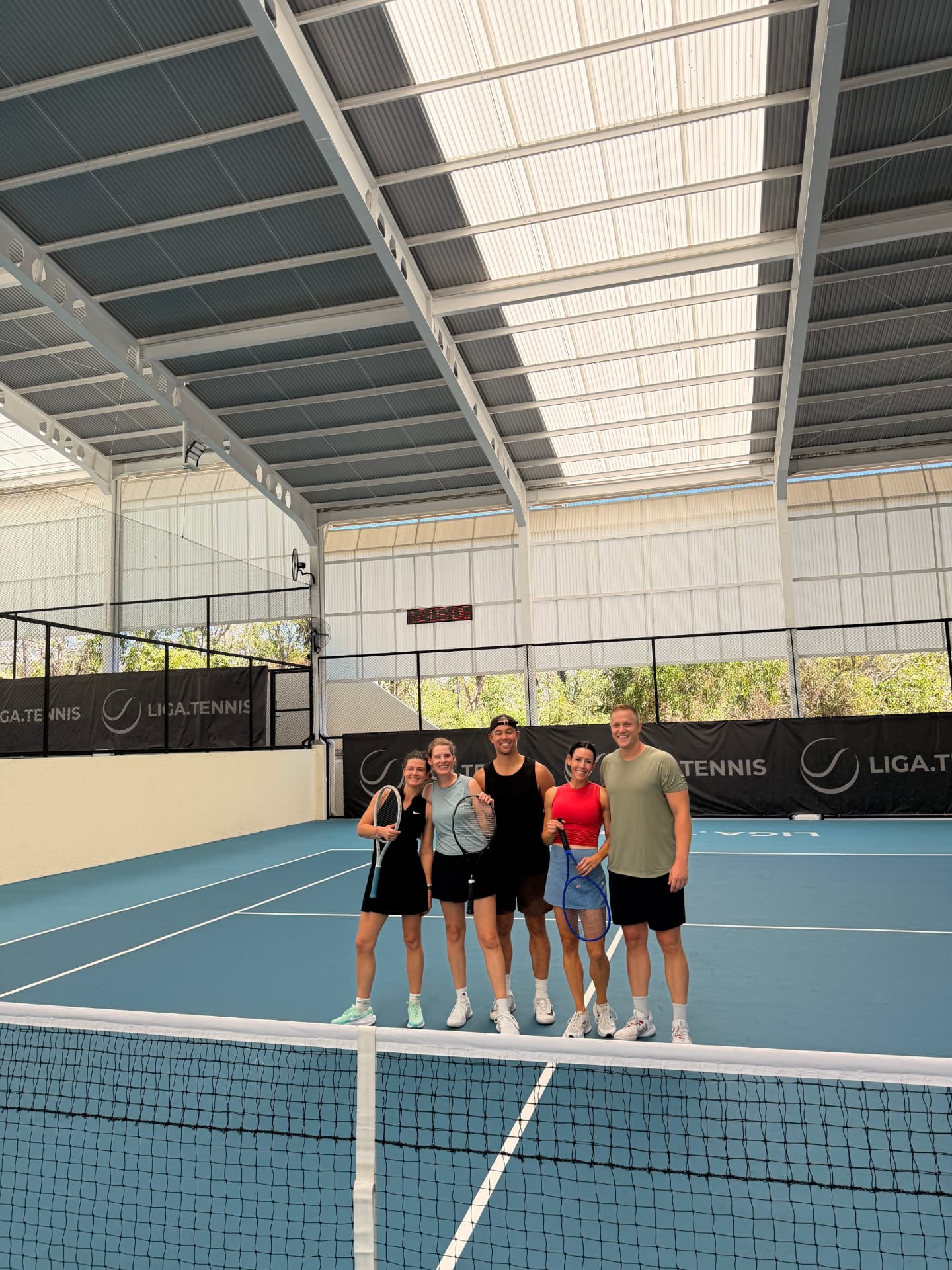 Five players posing together at the net on an indoor blue court