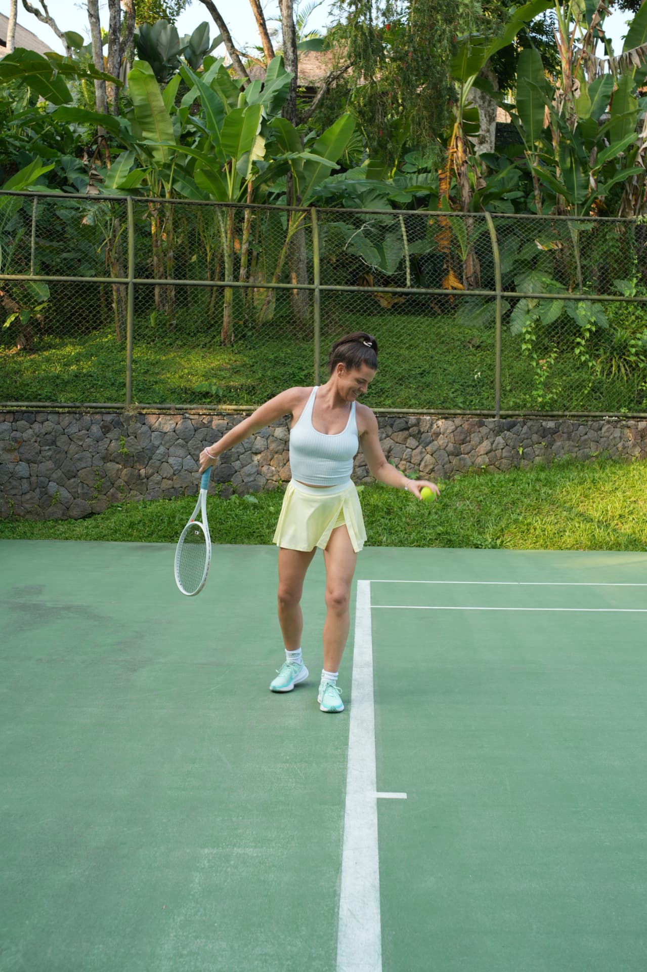 A player on a green tropical tennis court holding a racquet and a ball